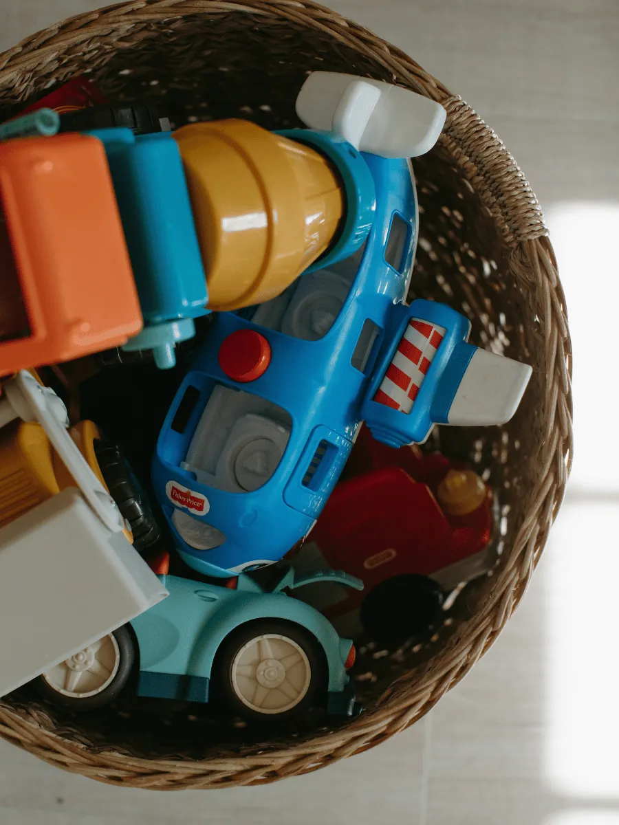 Overflowing toy basket with many toys piled together on a playroom floor