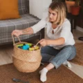 A woman on the living room floor holds up a woven basket of kids' toys: toy rotation