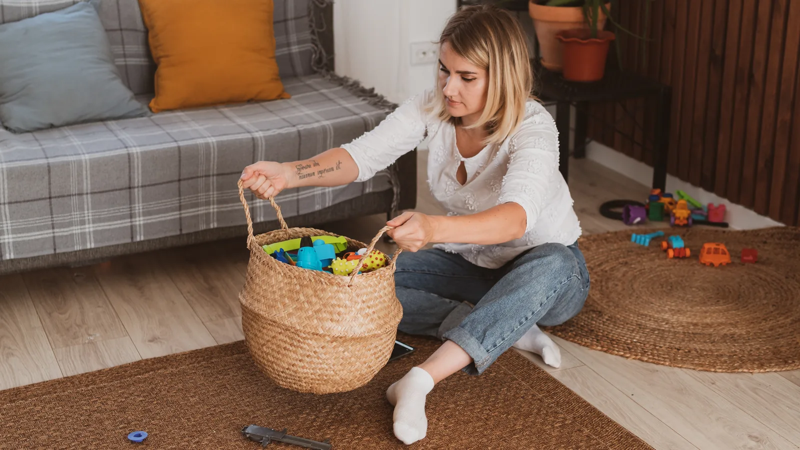 A woman on the living room floor holds up a woven basket of kids' toys: toy rotation
