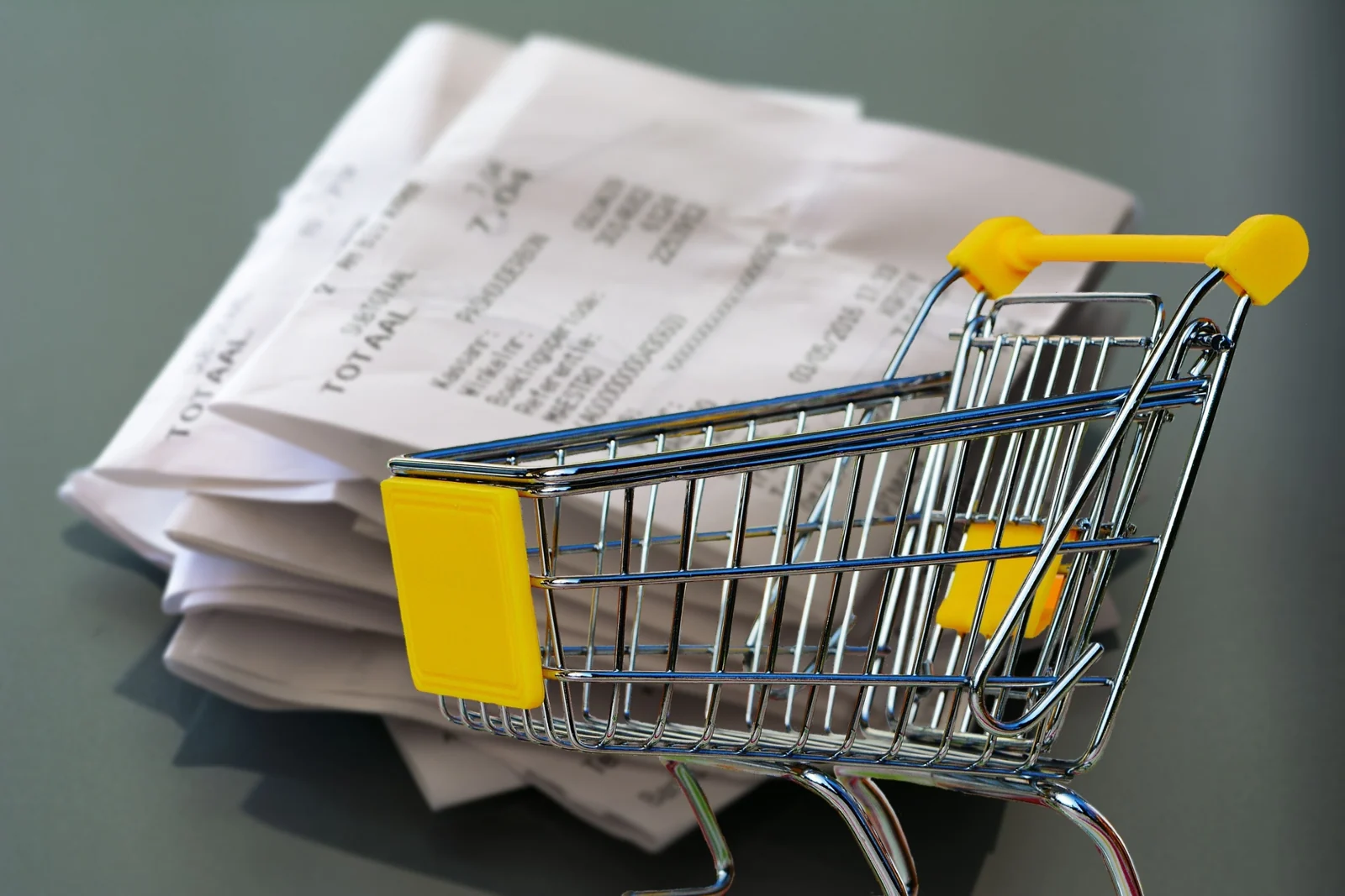 Miniature shopping cart parked in front of a pile of long paper receipts