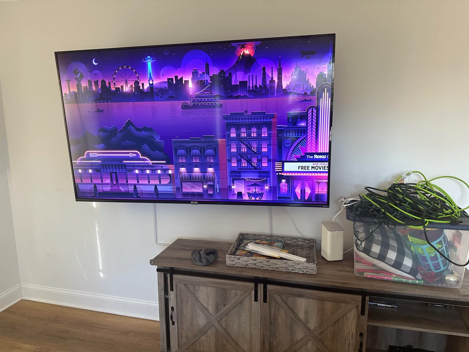 A wall-mounted TV with thin white cord covers running down the wall to the media console below
