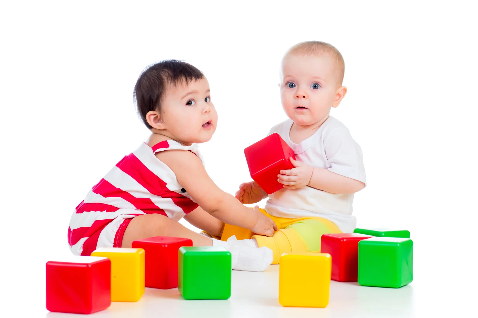 Two babies sitting side by side, playing with large colorful blocks
