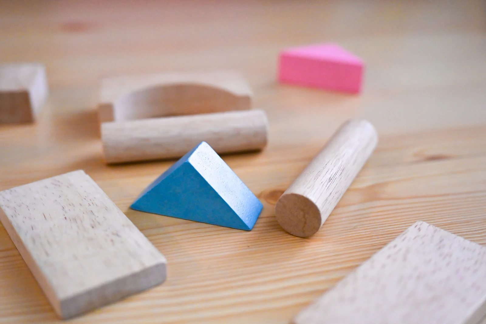 Plain wooden blocks and a round dowel beside a blue and a pink painted piece on a light wooden table