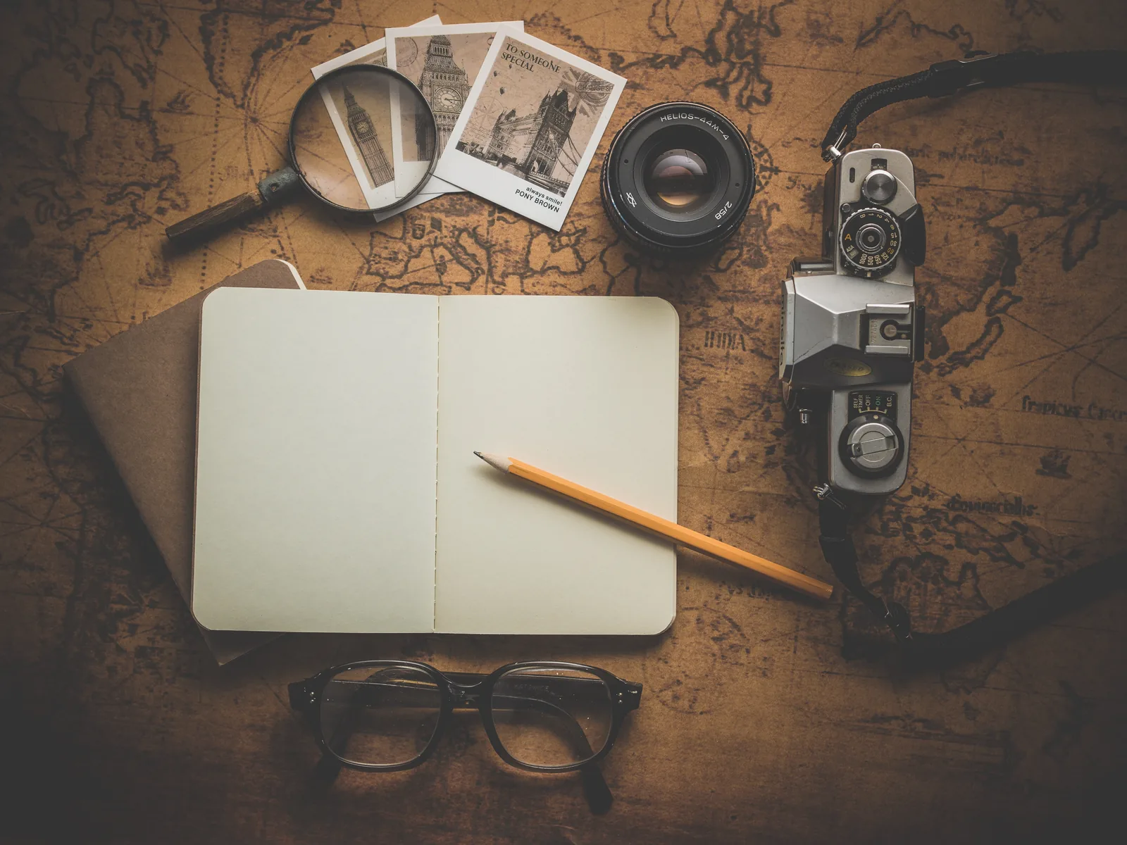 Vintage world map spread across a wooden desk with old books and a magnifying glass