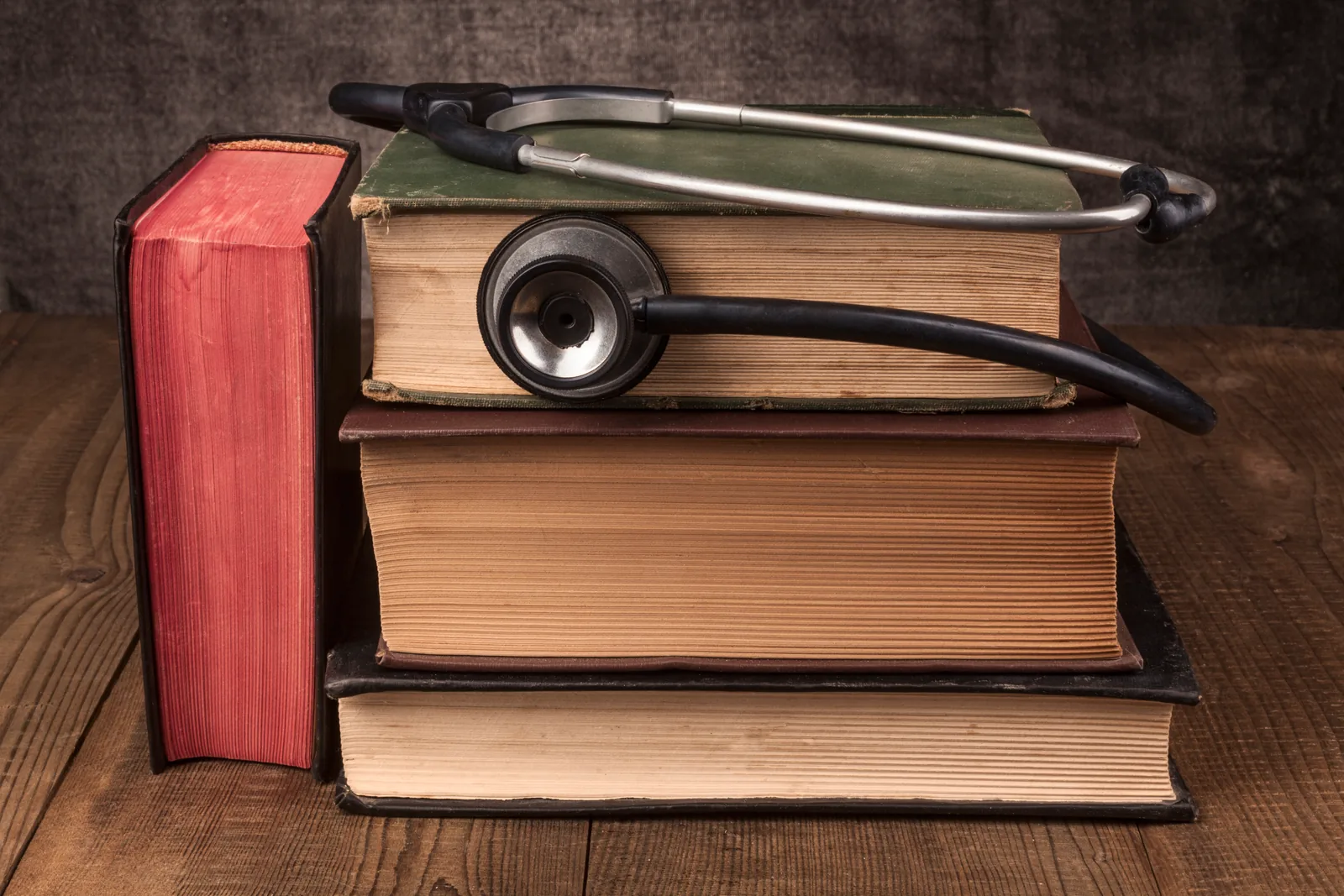Vintage stethoscope resting on a stack of old cloth-bound books on a wooden desk