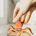 A hand lifts a small painted wooden octopus toy from a sunlit table, checking what makes a toy Montessori