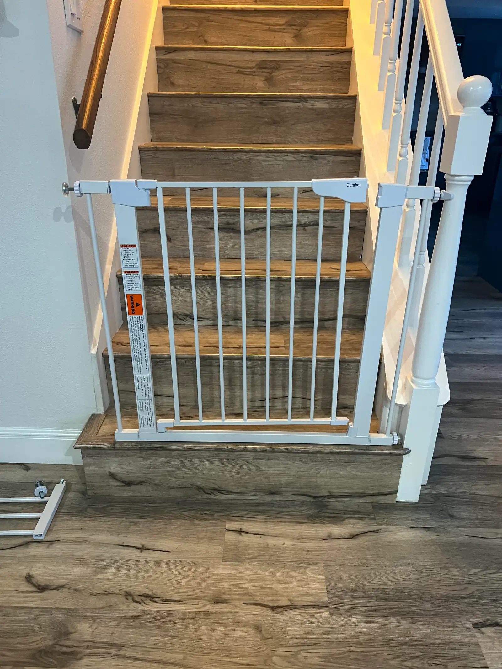 A white metal safety gate fitted across the bottom of a wooden staircase