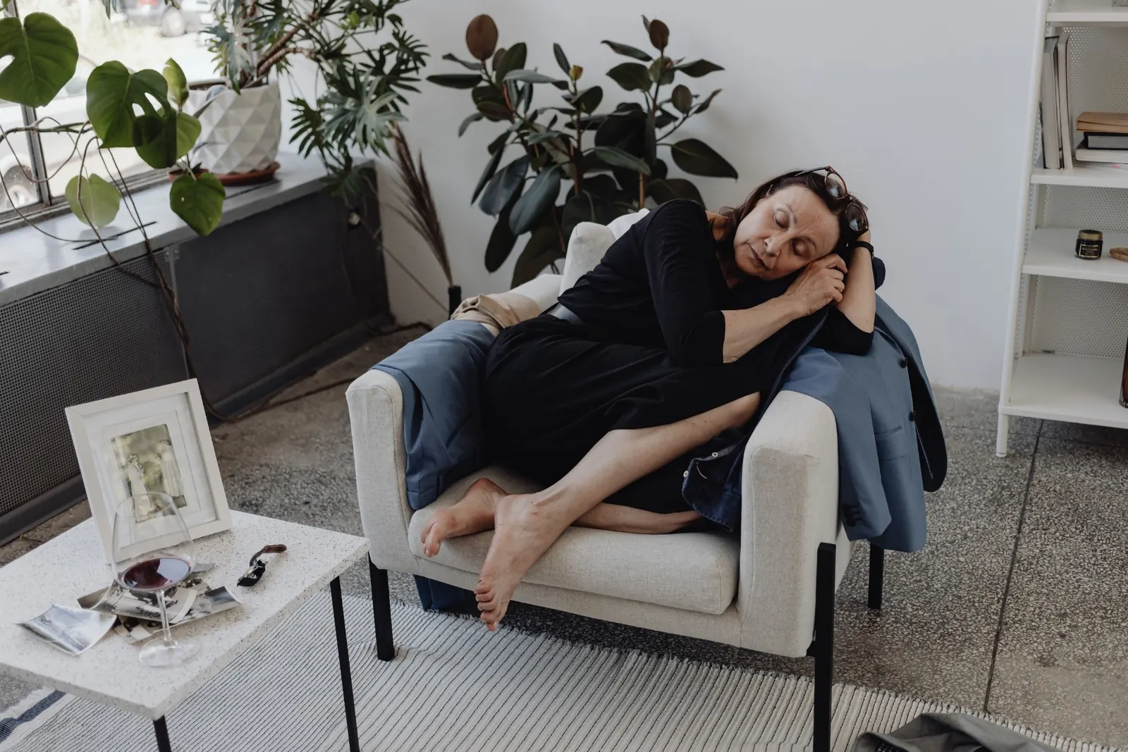 A woman naps curled up in an armchair in a bright, quiet living room