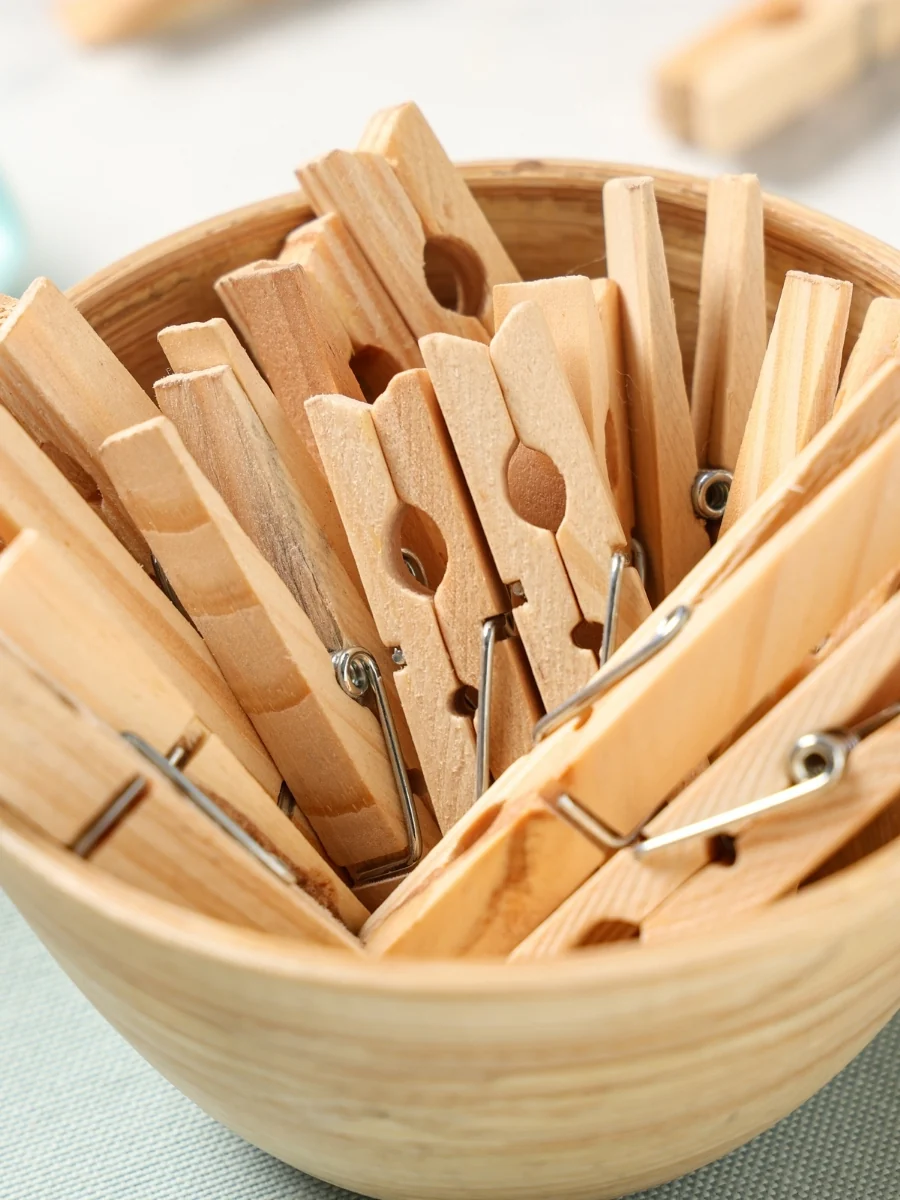 Wooden clothespins piled in a wooden bowl on a green cloth