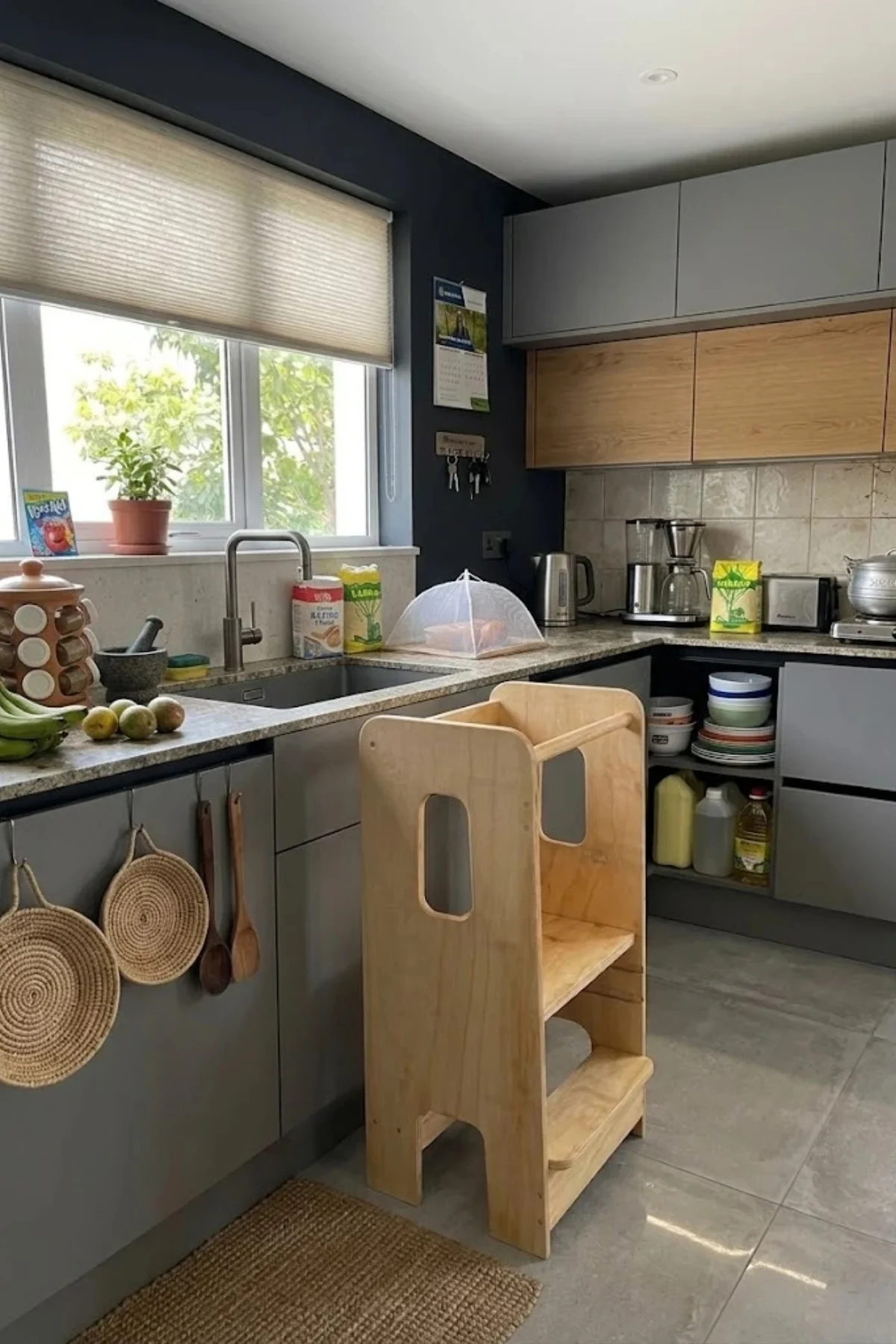 An empty wooden learning tower with cut-out sides standing at a kitchen counter next to the sink