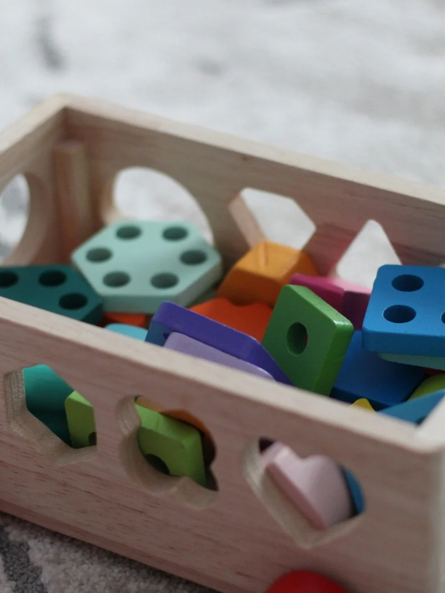 Wooden shape sorter box filled with chunky colored shapes, each cut to fit only one hole