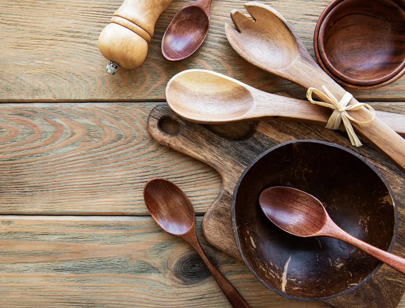 Wooden spoons, wooden bowls, a cutting board and a pepper mill on a rustic wooden table