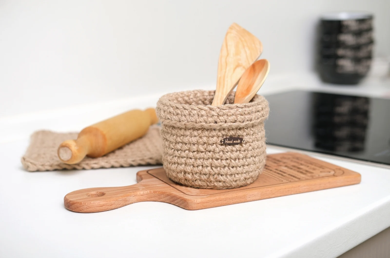 Woven rope basket holding wooden spoons, next to a rolling pin and a cloth napkin on a kitchen counter