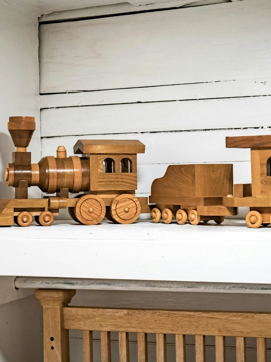 A wooden toy train sits on a white shelf ledge against a white wall