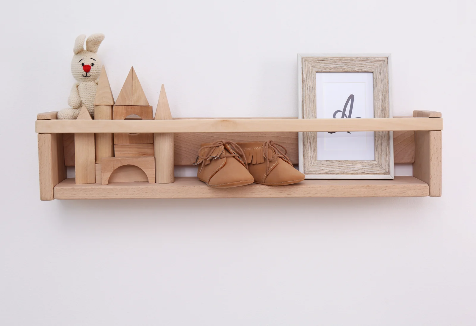 A small wooden wall shelf holding a plush bunny, wooden blocks, baby booties and a framed picture