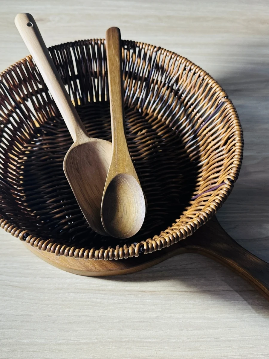Two wooden spoons resting in a woven basket on a wooden board