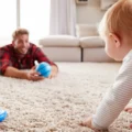A baby crawls across a soft rug toward a parent lying on the floor close by: a yes space