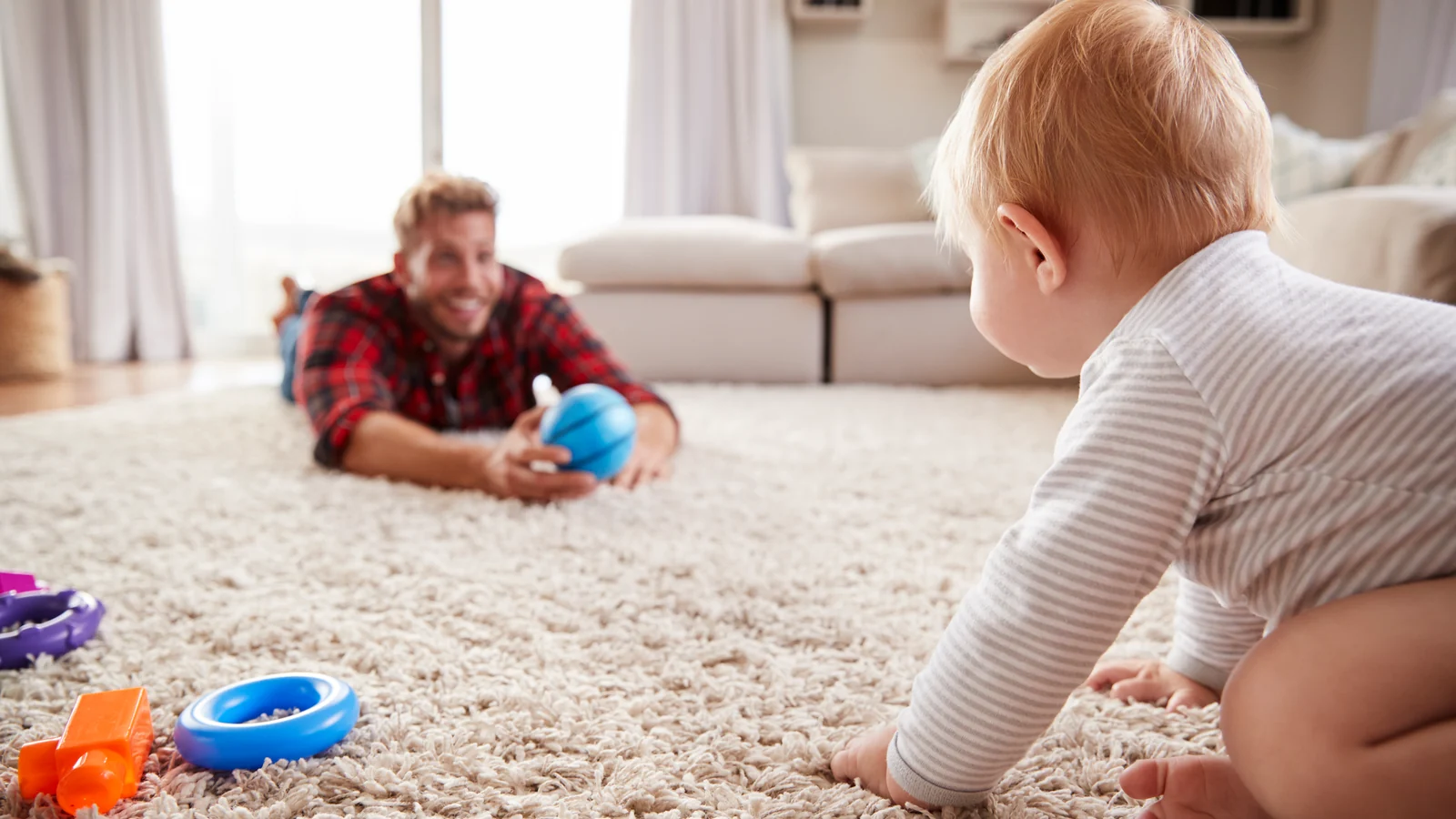A baby crawls across a soft rug toward a parent lying on the floor close by: a yes space